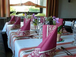 A dining table set with pink napkins, clear glasses, and a vase with purple flowers.