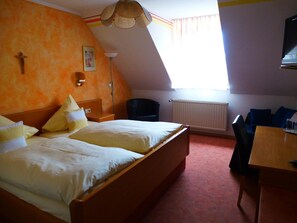 A hotel room with a large bed, a desk, a chair, a radiator, and a window with curtains.
