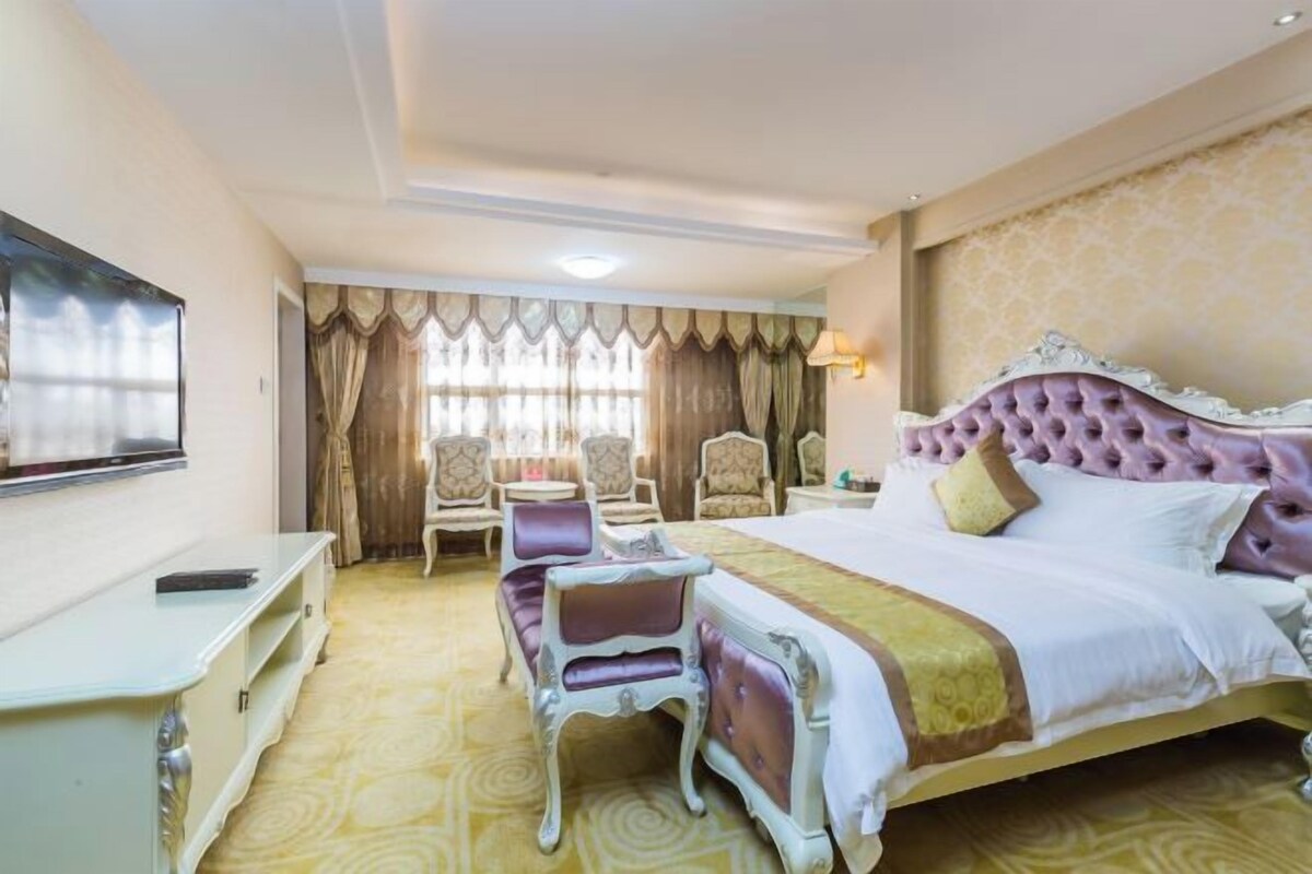 A hotel room with a large bed, a TV, a desk, and two chairs.