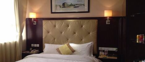 A hotel room with a large bed, a headboard, two bedside lamps, a nightstand with a phone, and a framed picture on the wall.