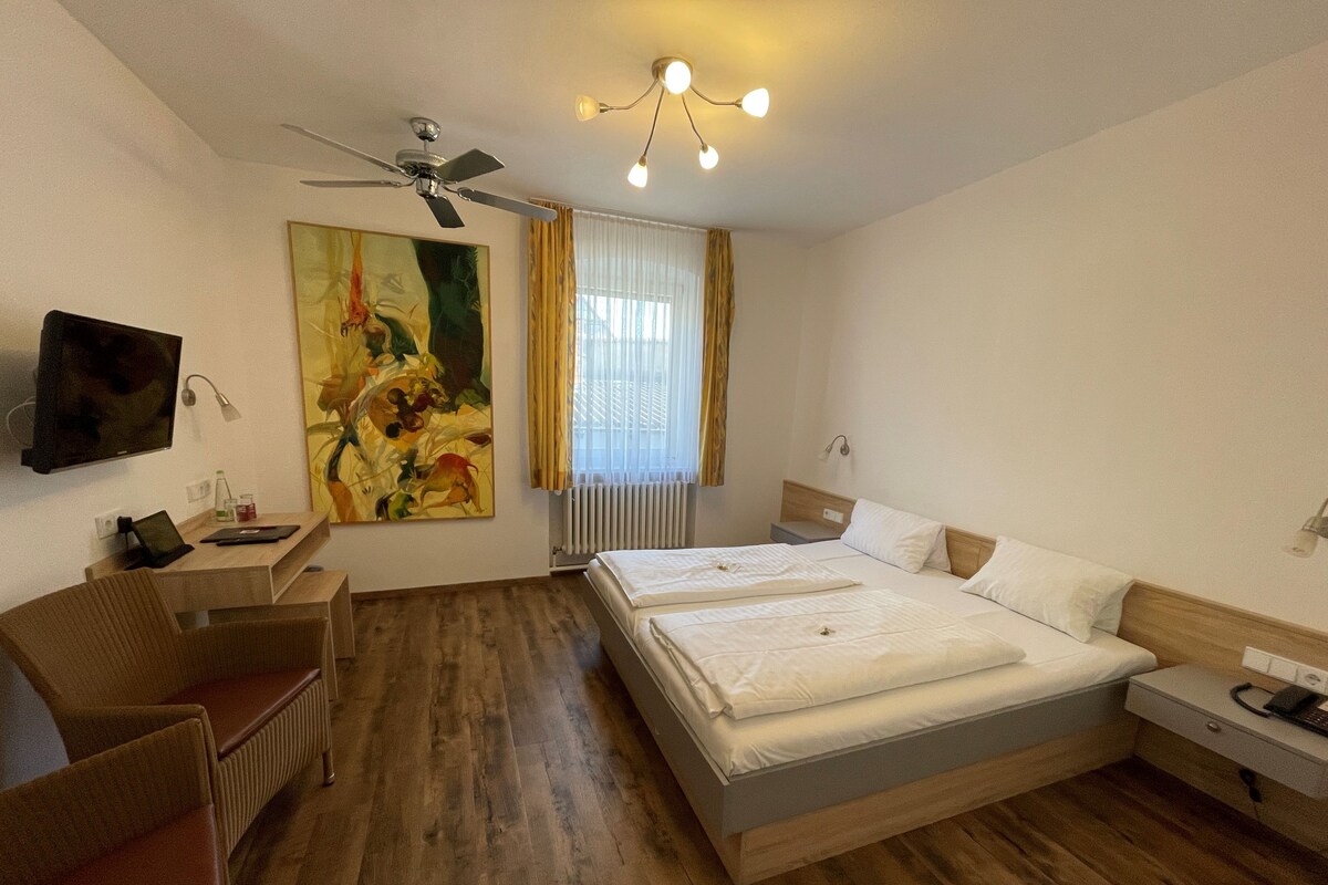 A hotel room with a bed, a desk, a chair, a television, and a painting.