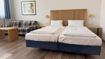 Een tweepersoonsbed met houten hoofdbord, een klein nachtkastje, een lamp en een bank met ruitkussens.