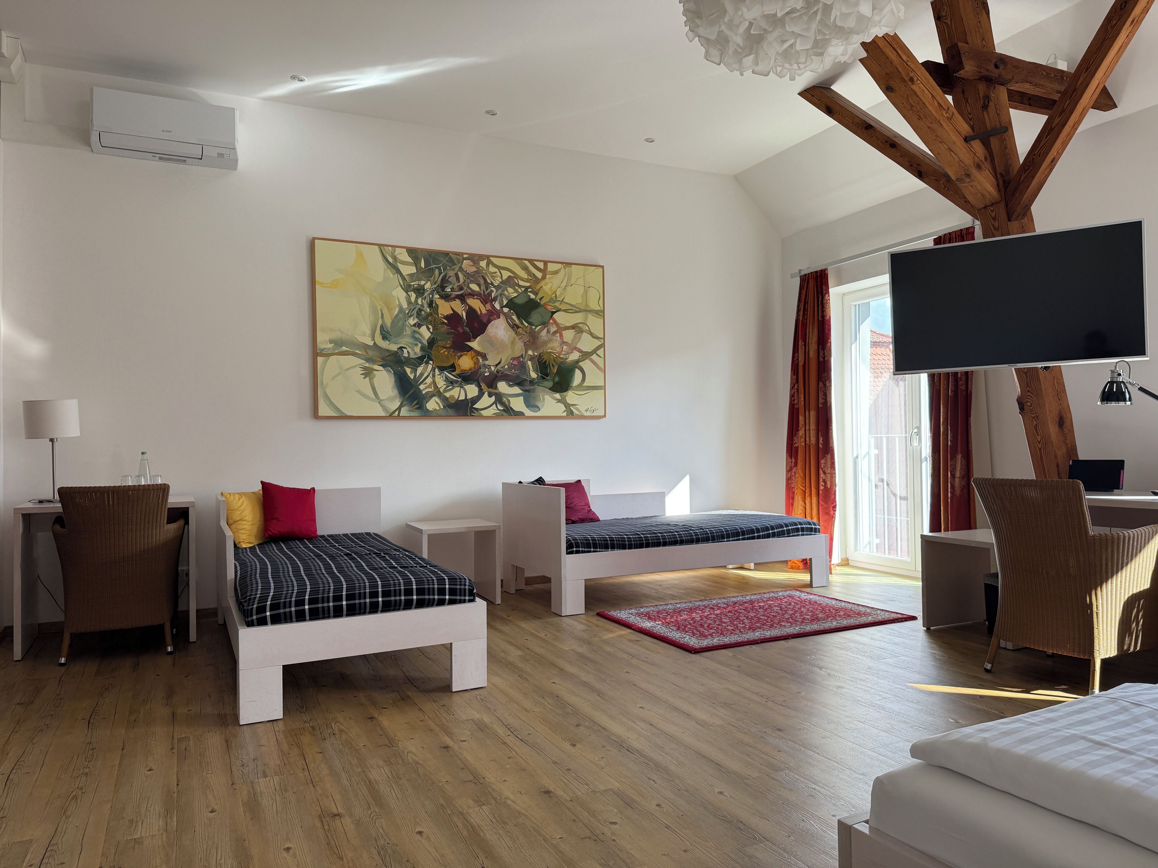 A modern room with two beds, a desk, a chair, a flat-screen TV, and a large abstract painting.