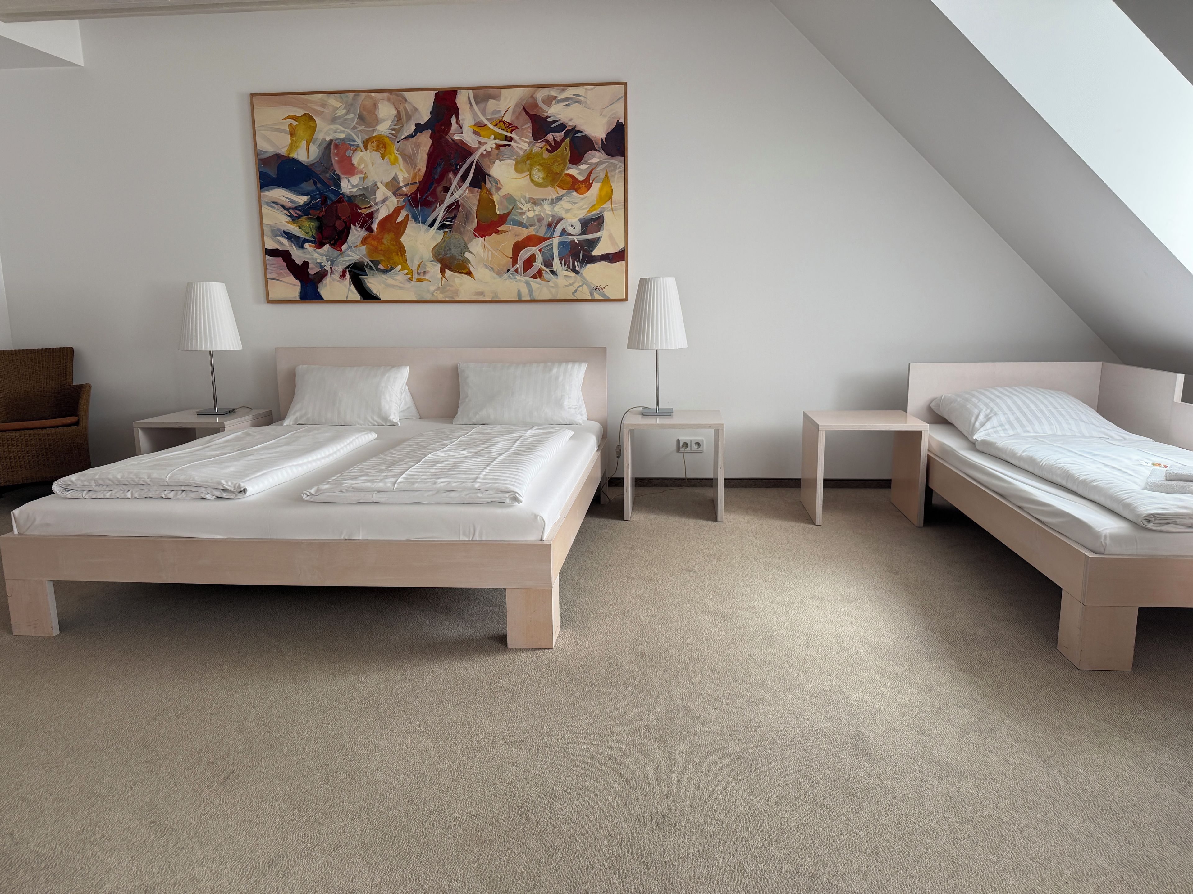 Un dormitorio moderno con una cama grande, dos mesitas de noche, una silla y un cuadro abstracto y colorido en la pared.