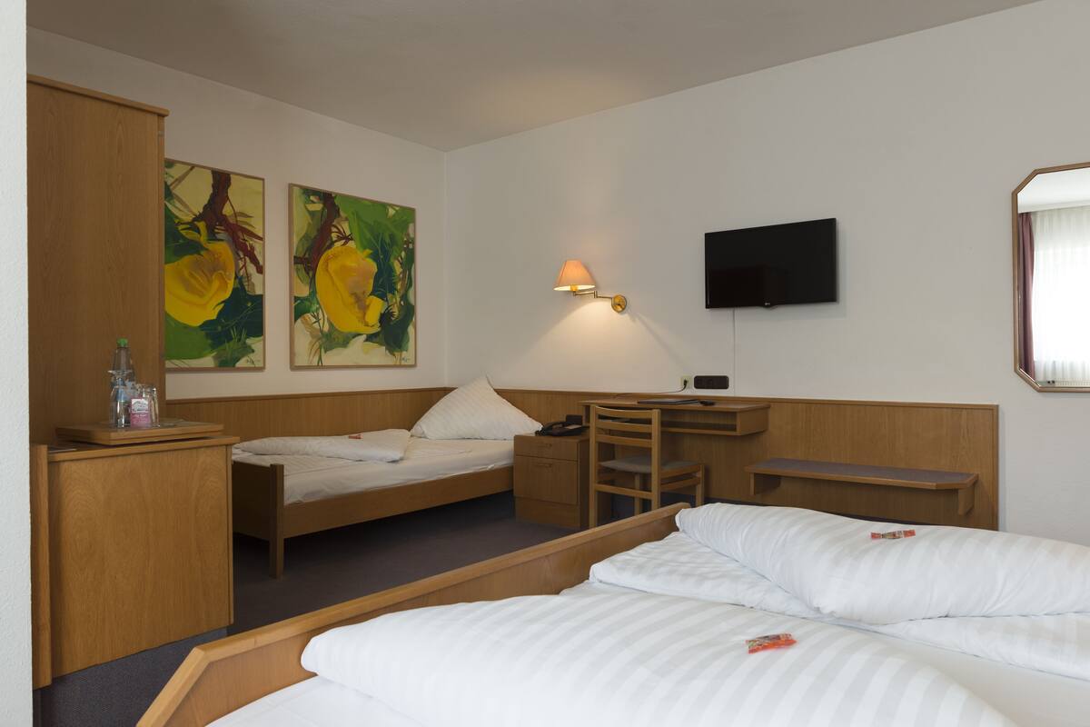Une chambre d’hôtel avec un lit, un bureau, une chaise et un téléviseur fixé au mur.