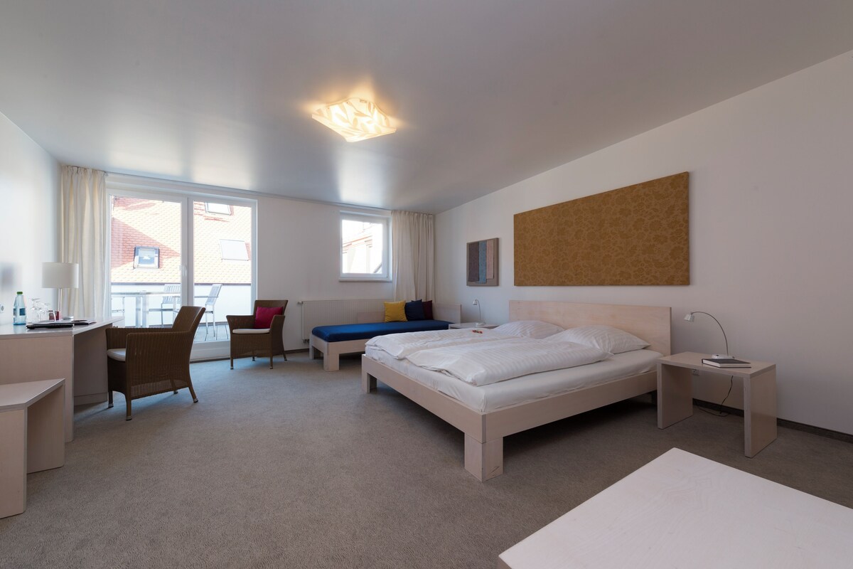 A hotel room with a bed, a desk, a chair, a sofa, and a window.