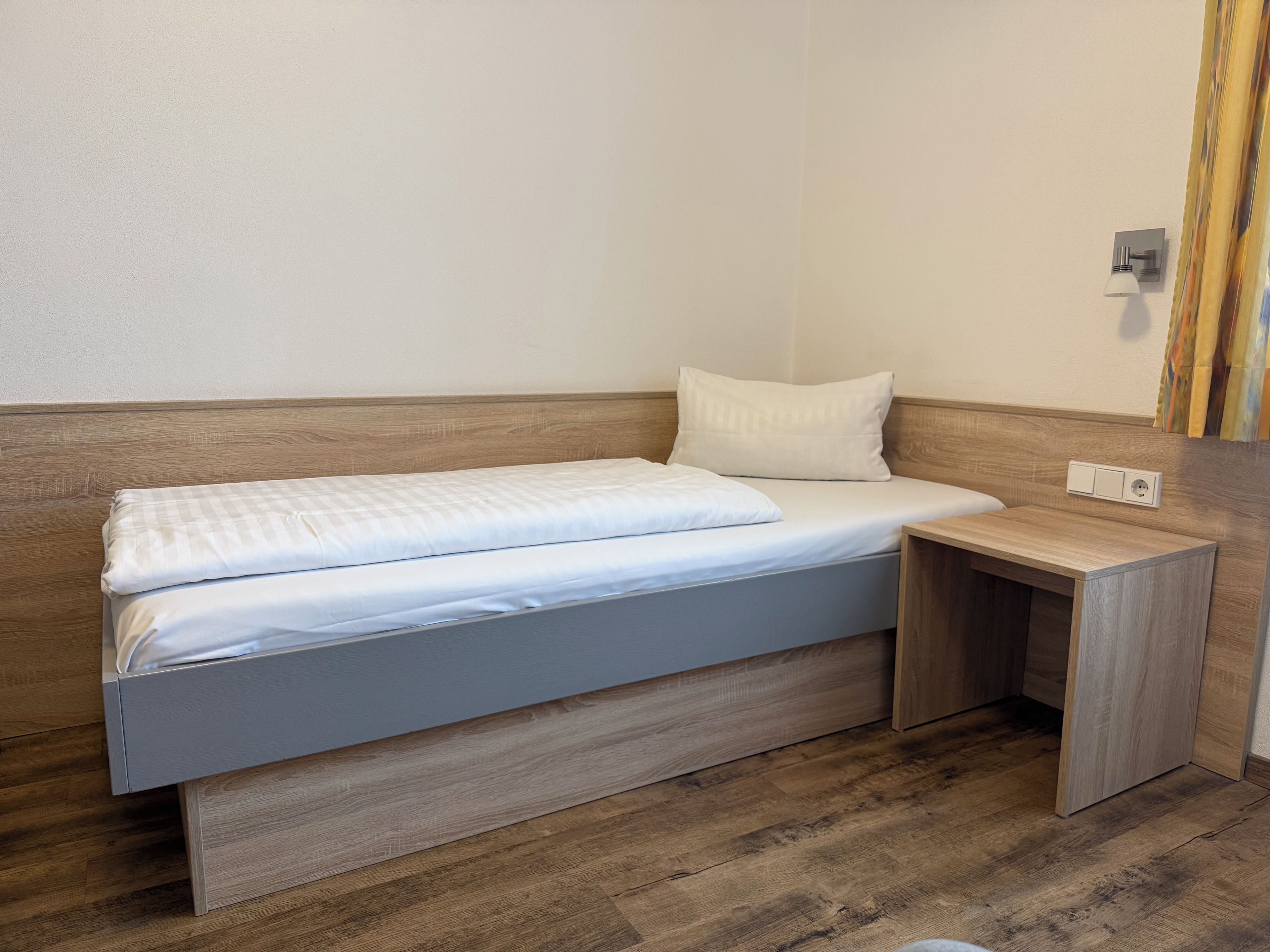 Een enkel bed met een houten hoofdeinde en een nachtkastje.