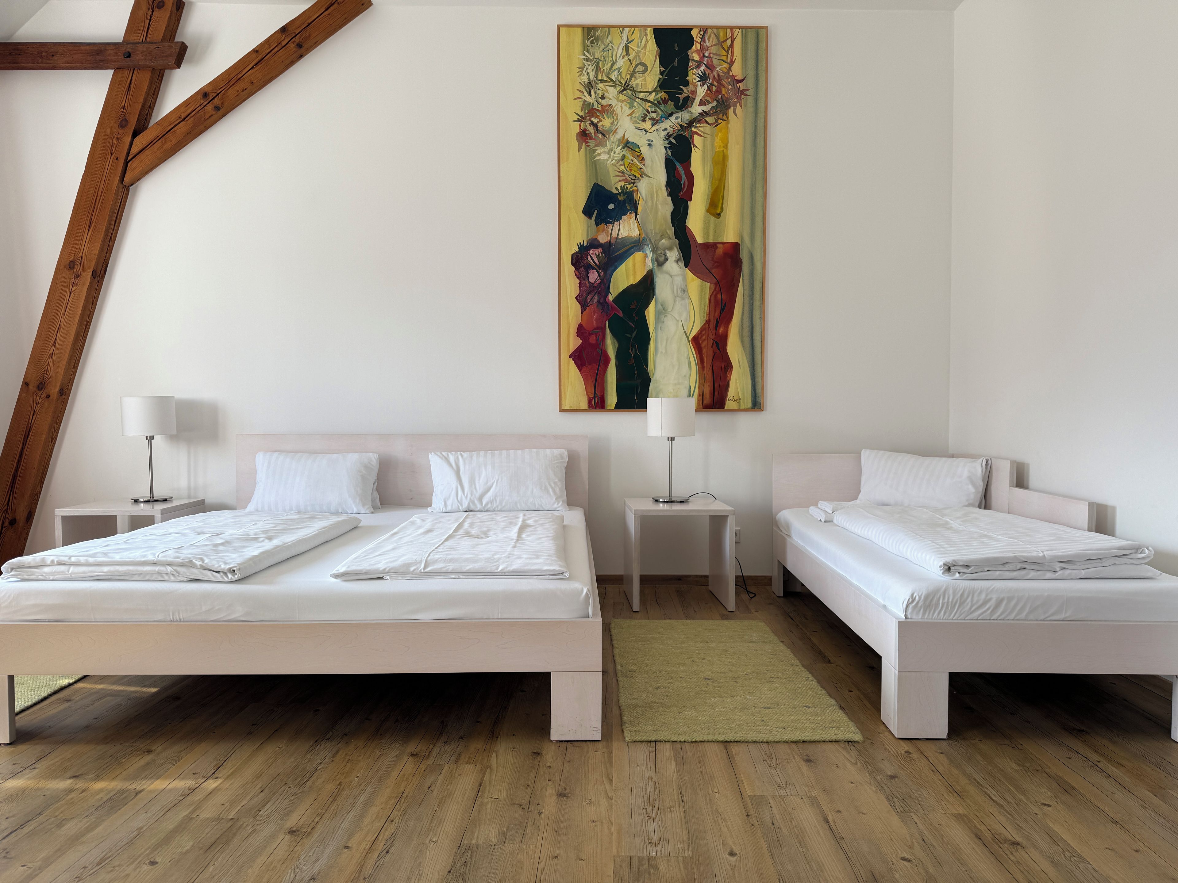 Habitación de hotel con dos camas, un cuadro abstracto grande y una viga de techo de madera.