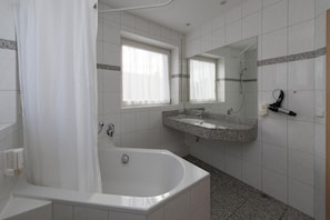 Un baño moderno con una bañera independiente, un tocador con encimera de granito y un espejo grande sobre el lavabo.