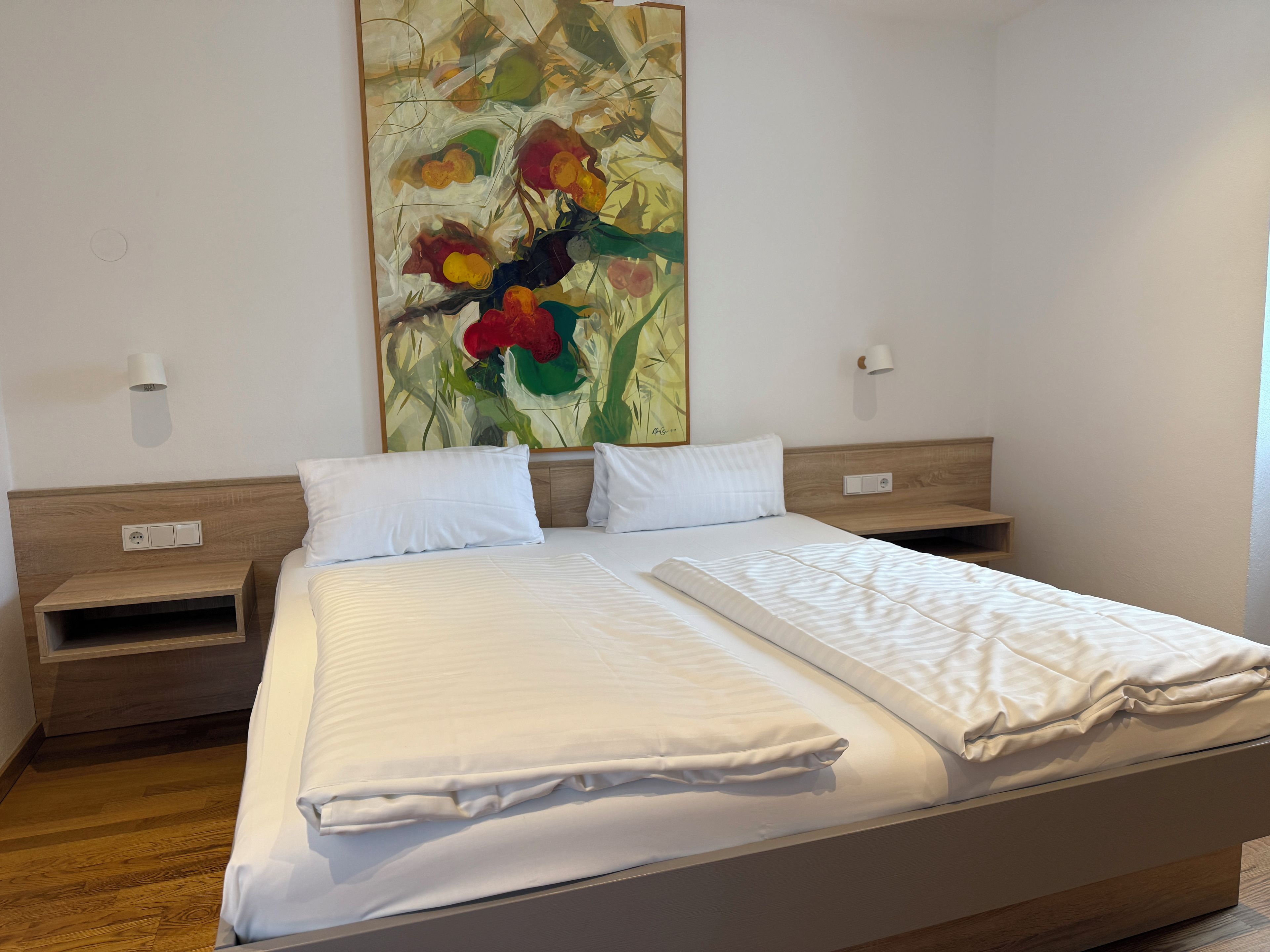 Ein Hotelzimmer mit einem großen Bett, zwei Nachttischen, einer Wandlampe und einem Gemälde.