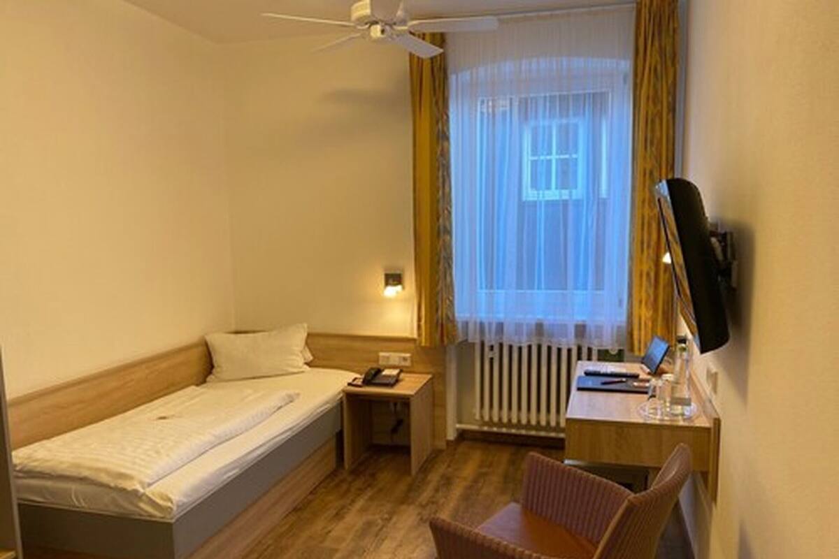 Une chambre d’hôtel avec un lit, un bureau, une chaise, une télévision et une fenêtre avec des rideaux.