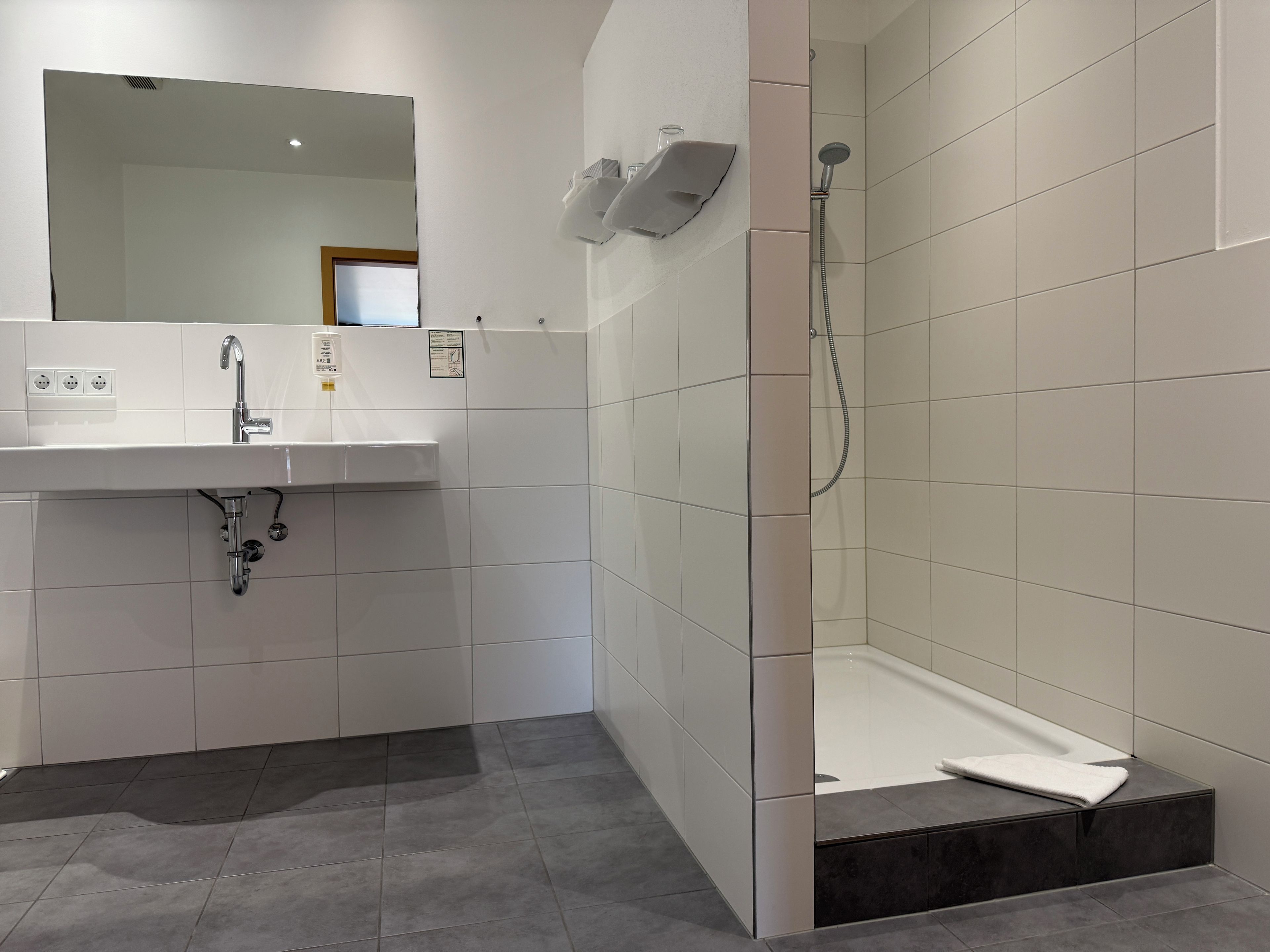 Un baño moderno con lavamanos, espejo y ducha blancos.