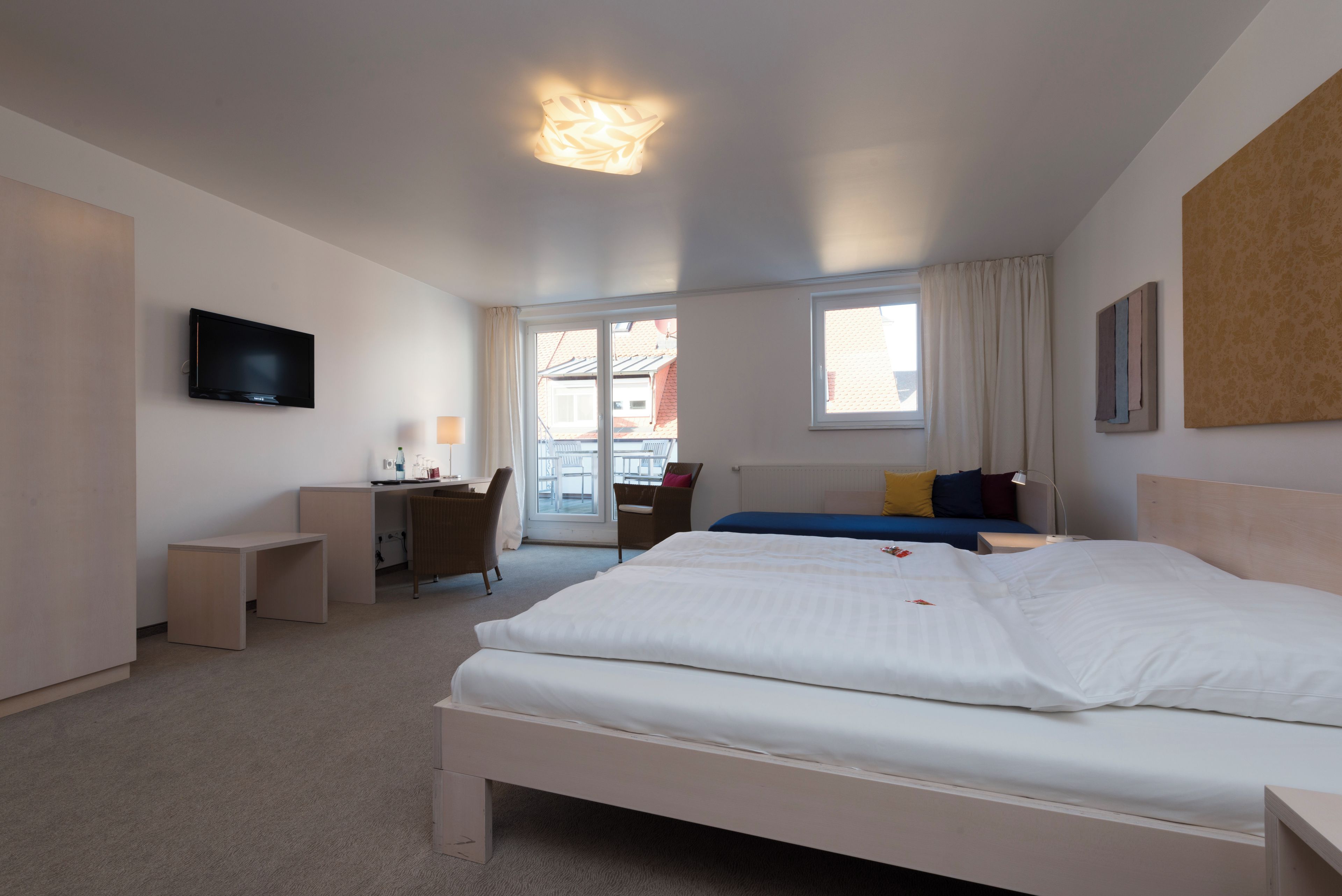 Ein Hotelzimmer mit Bett, Schreibtisch, Stuhl, Fernseher und einem Fenster mit Vorhängen.