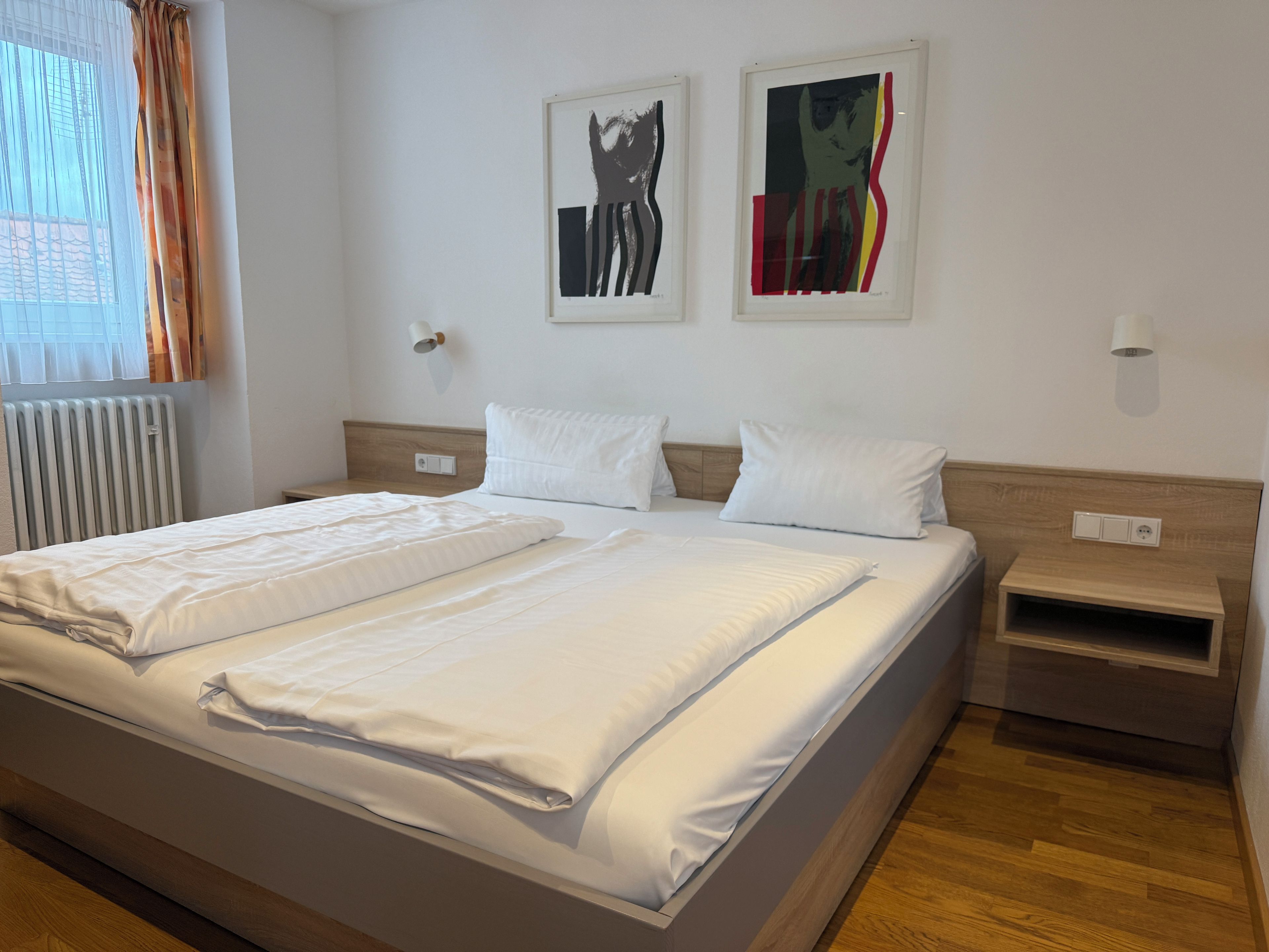 A hotel room with a large bed, two bedside tables, and two wall-mounted artworks.