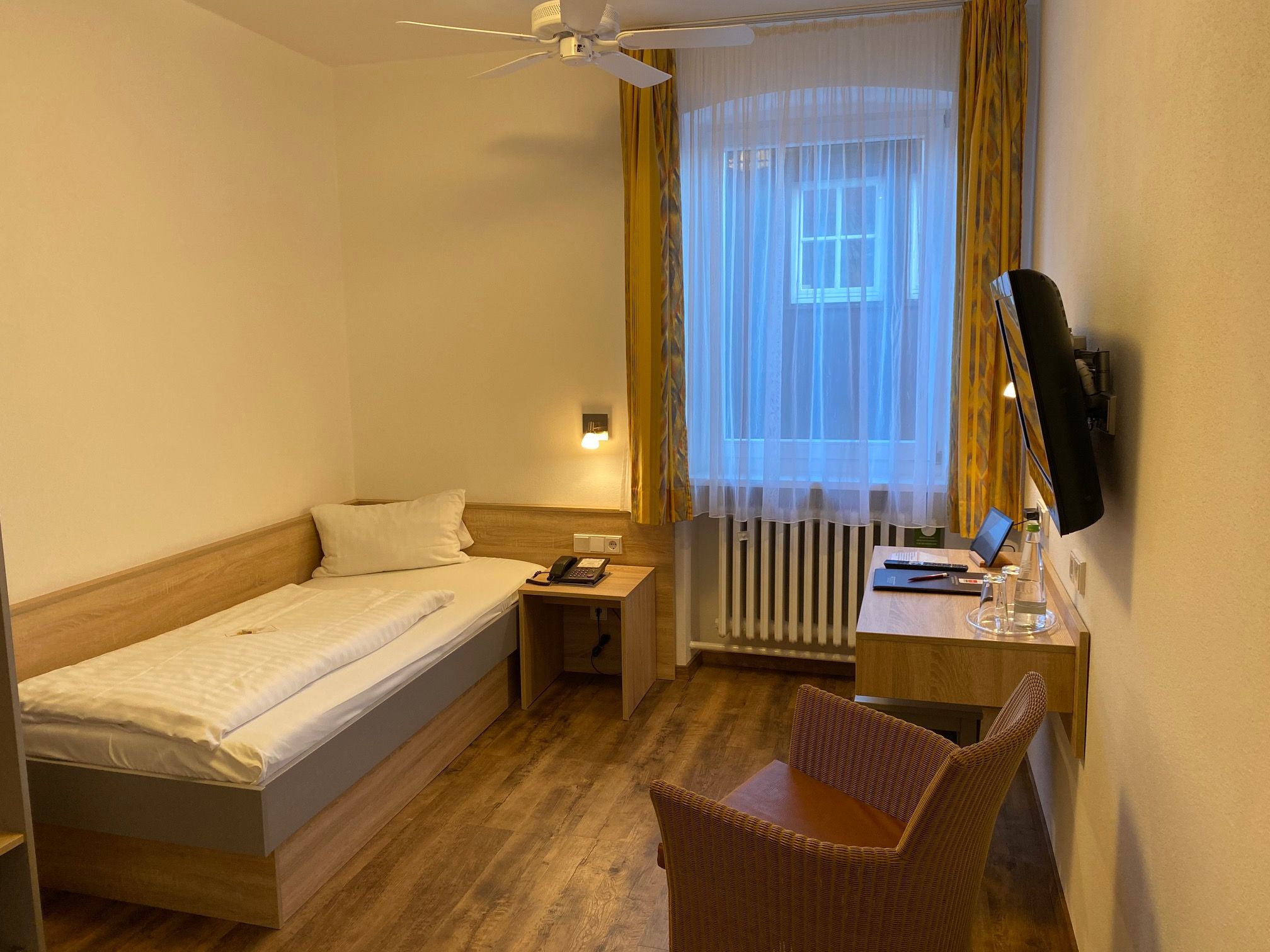 A hotel room with a single bed, a desk with a chair, a telephone, and a television mounted on the wall.