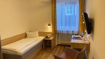 A hotel room with a single bed, a desk with a chair, a telephone, and a television mounted on the wall.