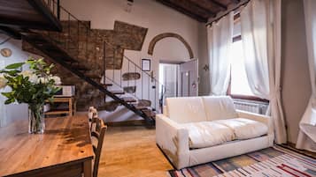 A cozy living room with a wooden dining table, a white sofa, and a staircase with stone walls.