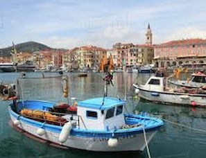 A harbor with boats docked, a building with a tower, and a mountainous backdrop.