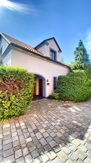 A two-story building with a tiled roof, a paved driveway, and a well-maintained hedge.