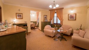Habitación de hotel con comedor, un conjunto de sofás, una araña y cuadros en las paredes.