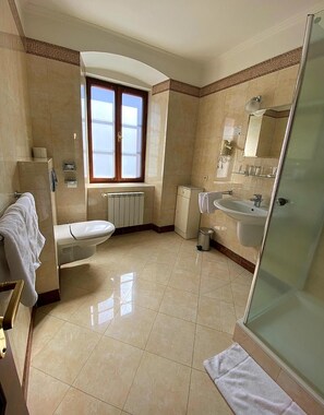 A bathroom with a toilet, sink, and shower area, featuring tiled floors and a window.