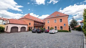 Un patio con zona pavimentada, un edificio de techo rojo y coches aparcados.