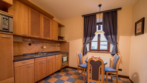 Una cocina con armarios de madera, encimera negra, horno integrado y una zona de comedor con dos sillas a rayas.