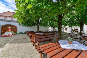 An outdoor seating area with wooden benches and tables, a traditional tent, and a building in the background.