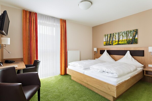A hotel room with a bed, a desk, a chair, a TV, and a painting on the wall.