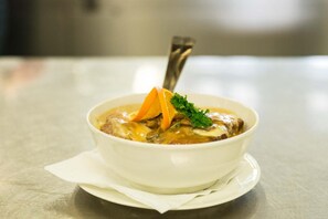 A white bowl of soup with a spoon, placed on a white napkin on a metal table.