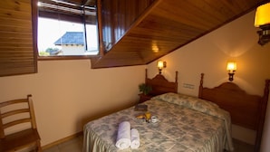 A bedroom with a wooden headboard, a bed with a floral bedspread, two rolled towels, a bedside table with a lamp, and a window with blinds. - Casa Francho (Laspaules)