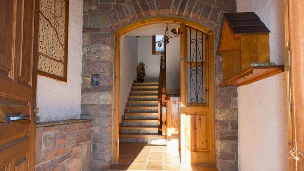 A stone staircase leading to a wooden door with a metal gate, a wooden shelf, and a wall-mounted light fixture. - Casa Francho (Laspaules)