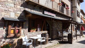 A stone building with a wooden balcony, outdoor seating, and flower pots. - Casa Francho (Laspaules)