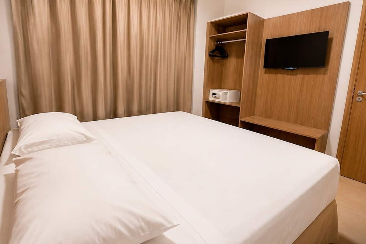 A hotel room with a bed, a television mounted on the wall, and a microwave on a wooden shelf.