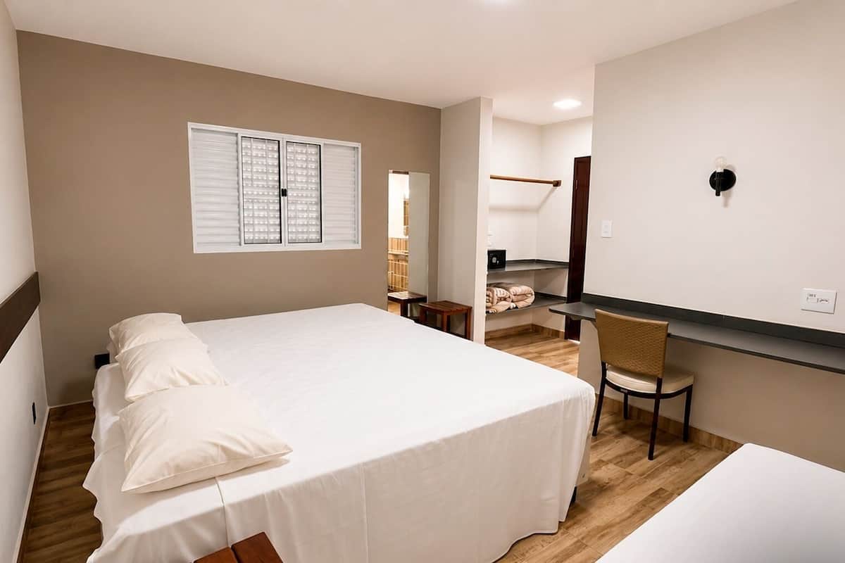 A bedroom with a bed, a chair, a desk, a wardrobe, and a window with blinds.