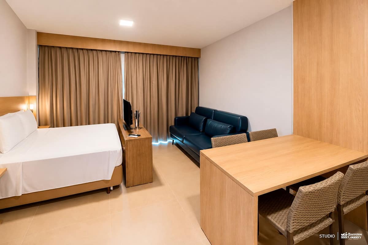 A hotel room with a bed, a sofa, a dining table, and a TV on a wooden stand.