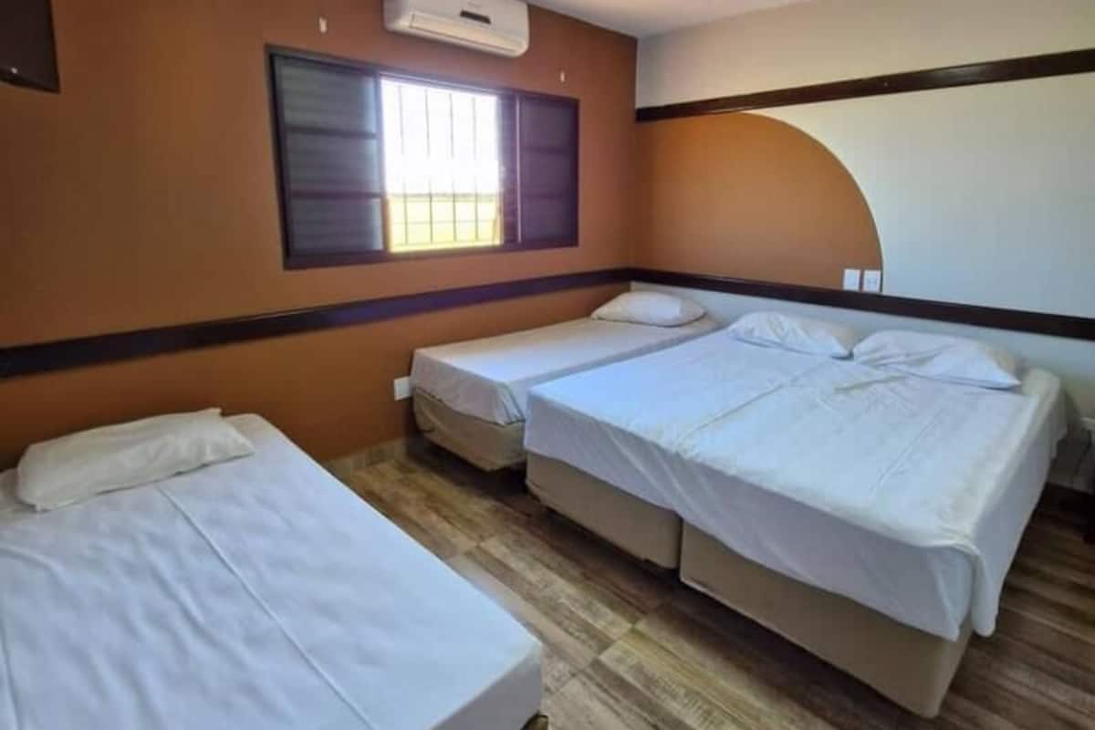 A hotel room with two beds, a window with blinds, an air conditioning unit, and a curved wall.