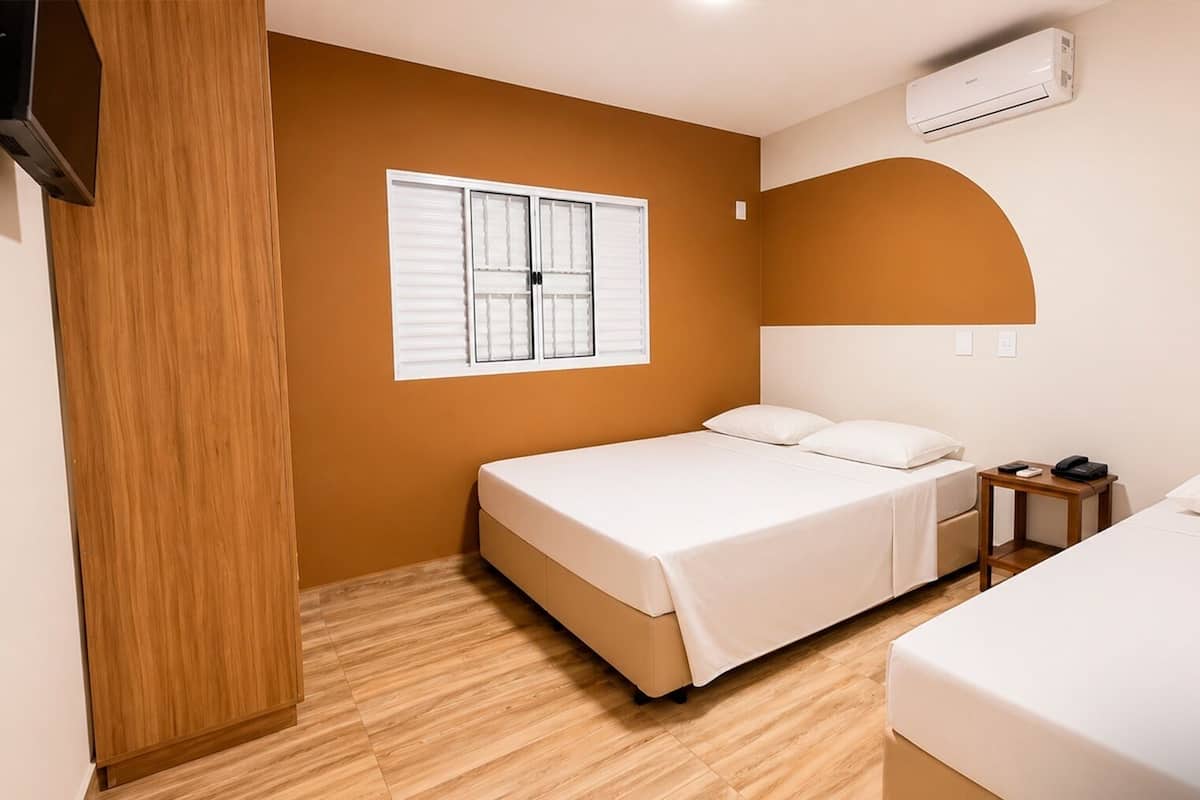 A hotel room with a bed, bedside table, and an air conditioning unit.