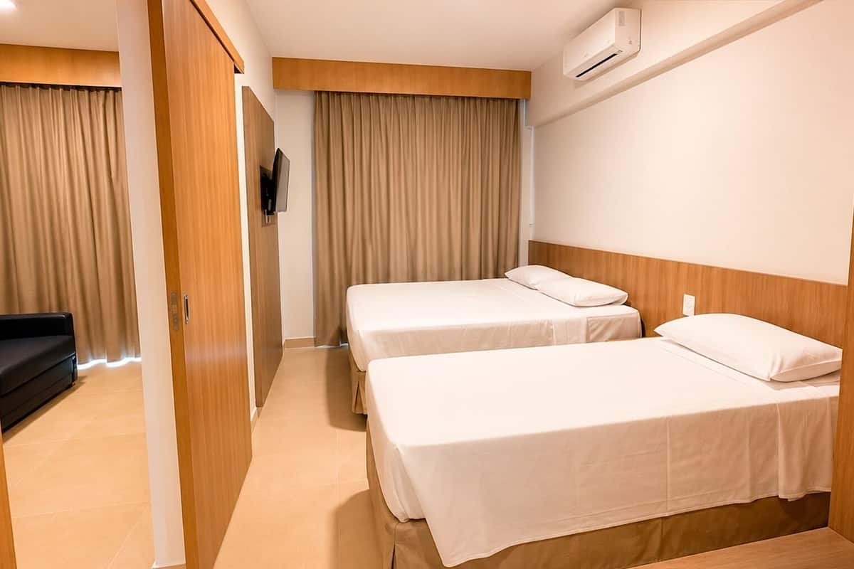 A hotel room with two beds, a TV, an air conditioner, and a sofa.