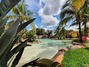 Een tropisch resort met een helder zwembad, palmbomen en een waterval.