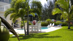 Area piscina con tavolo e sedie, circondata da palme e un prato curato.