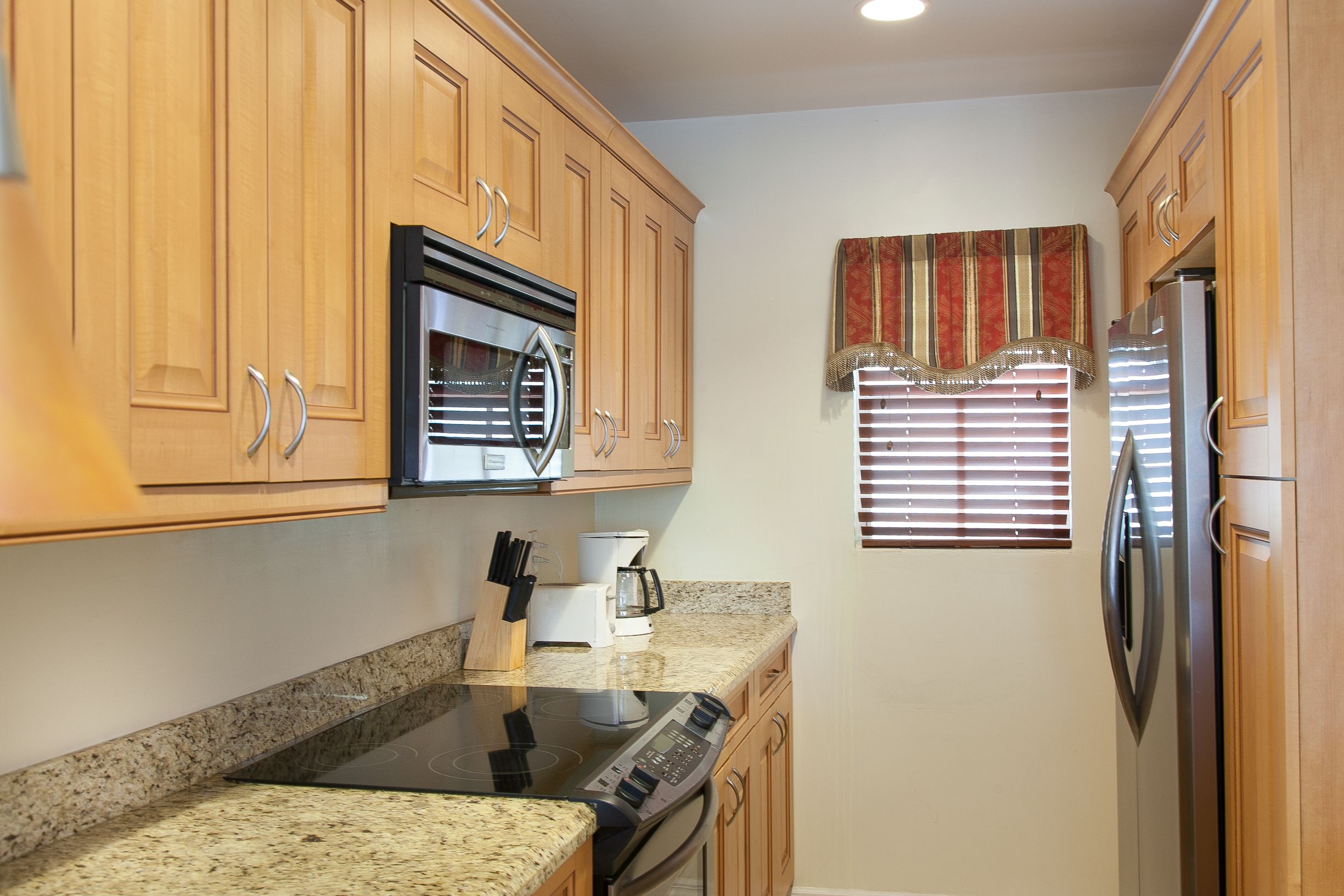 A kitchen with wooden cabinets, a stainless steel refrigerator, a built-in oven, and a granite countertop.