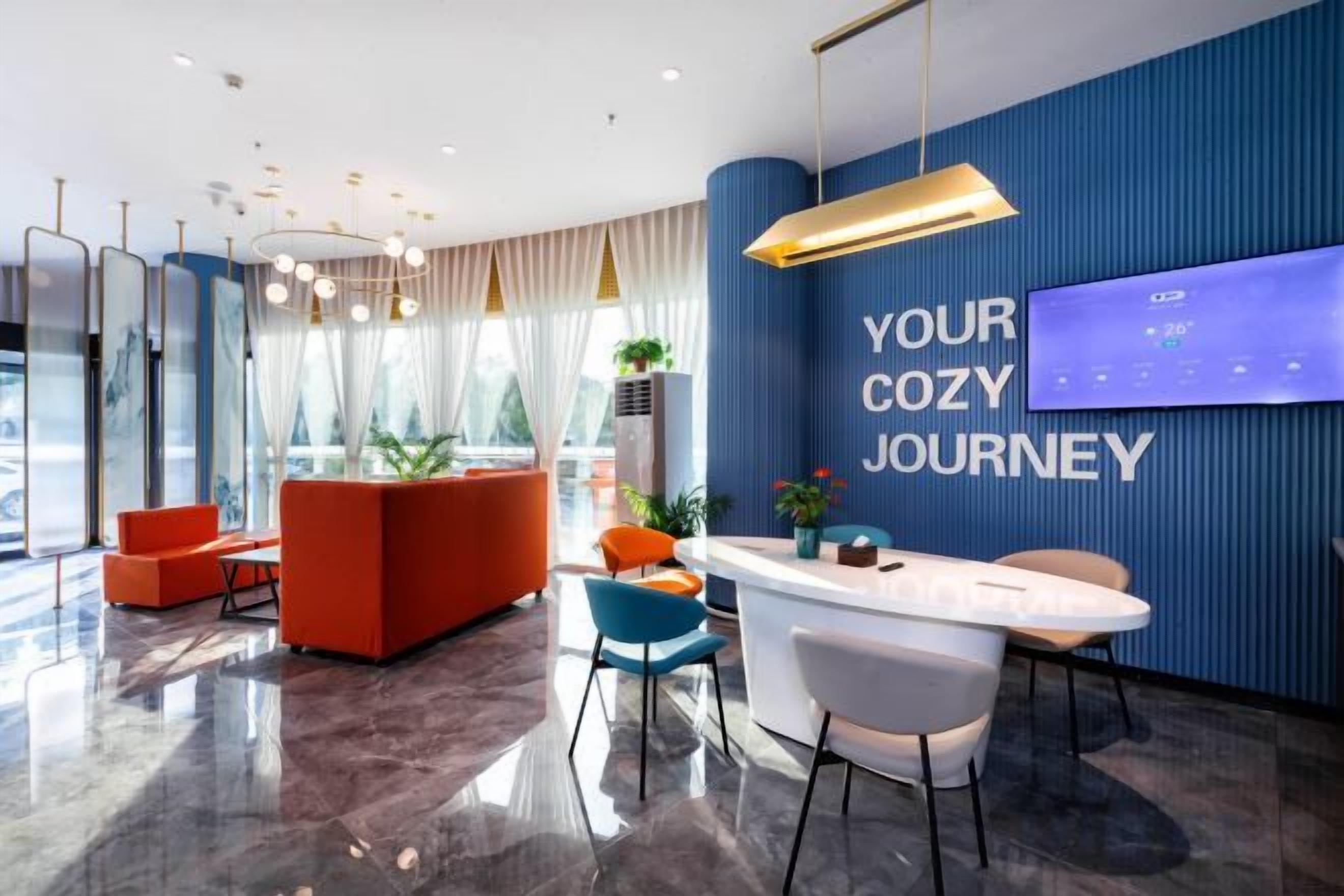 A modern hotel lobby with a reception desk, seating area, and a large digital display on the wall.