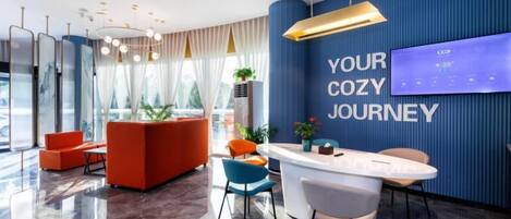A modern hotel lobby with a reception desk, seating area, and a large digital display on the wall.
