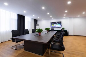 Un salón de conferencias con una larga mesa, sillas, una pantalla de televisión y plantas en macetas.