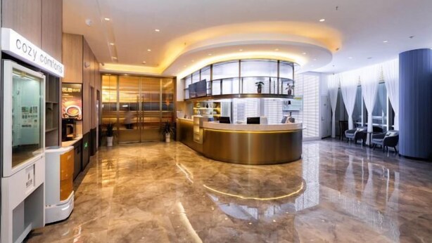 Eine moderne Hotelhalle mit Empfangstresen, Sitzgelegenheiten und einer Glastrennwand.