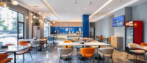 A modern restaurant with tables and chairs, a counter, and a television screen.