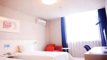 A hotel room with two beds, a desk, a chair, a red armchair, and a window with curtains.