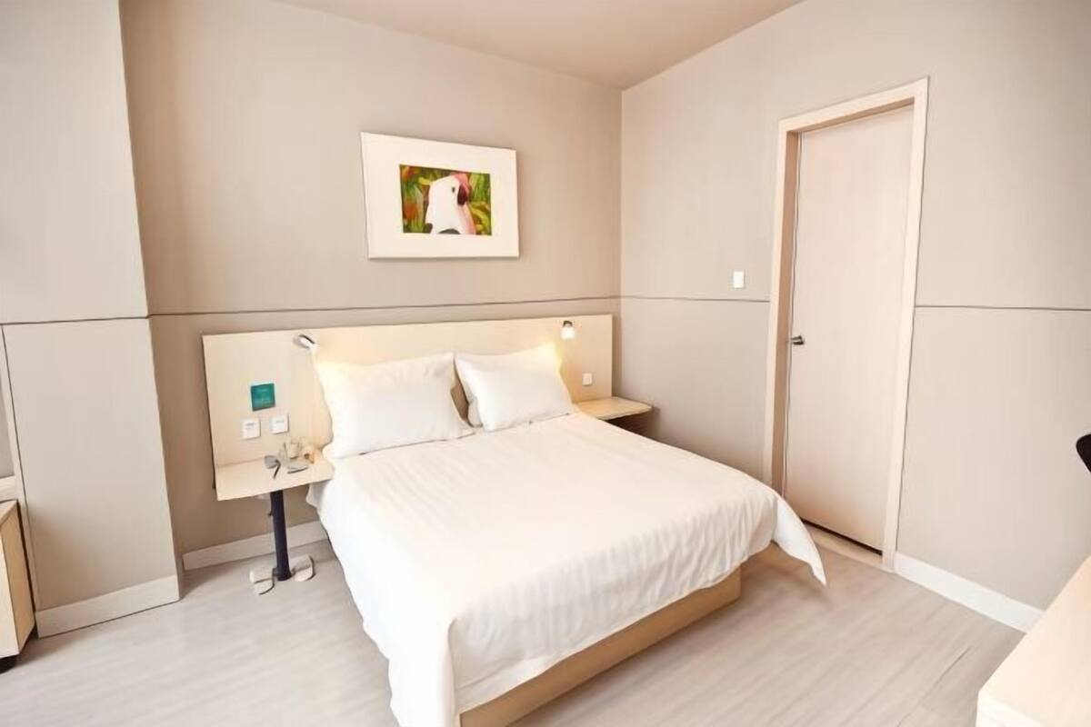 A hotel room with a bed, bedside tables, a nightstand, a wall-mounted picture, and a door.