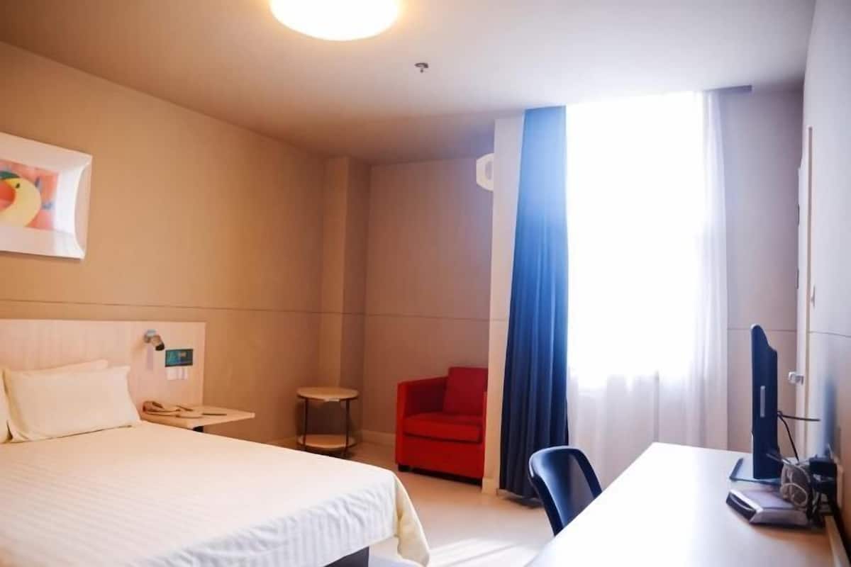 A hotel room with a bed, a desk, a chair, a small table, and a window with curtains.